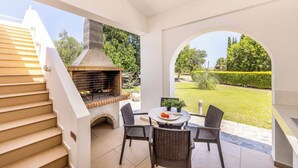 Eine Terrasse im Freien mit Kamin aus Ziegelsteinen, einem Esstisch mit Stühlen und Blick auf einen gepflegten Garten.