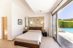 A bedroom with a stone wall, a bed, bedside tables, a mirror, and a view of a swimming pool.