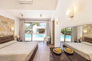 A hotel room with two beds, a pool view, stone walls, and a dining table with bananas.
