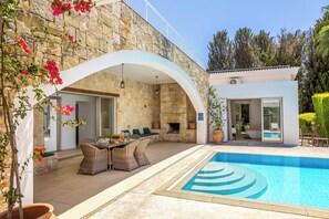 Un espace aménagé au bord de la piscine, avec un mur en pierre, des sièges d’extérieur et une piscine à l’eau d’un bleu limpide.