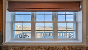 Una ventana con persiana enrollable marrón, tres vidrios y vista a una terraza con barandilla.