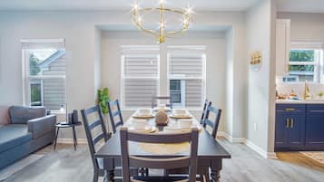 Un comedor con una mesa dispuesta para cuatro personas, sillas alrededor, una araña y una ventana con persianas.