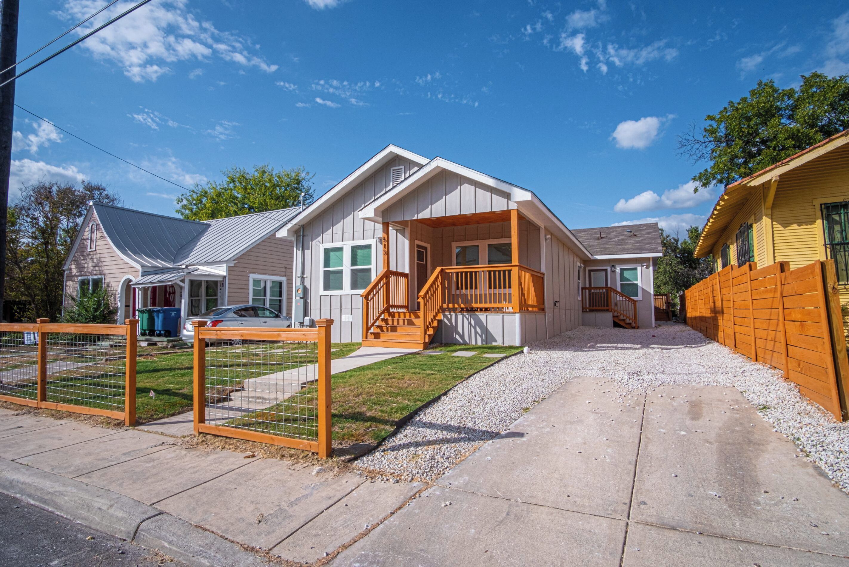 A two-story house with a front porch, a wooden staircase, and a fenced yard.