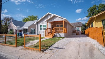 A two-story house with a front porch, a wooden staircase, and a fenced yard.