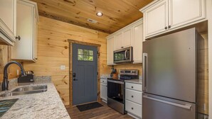 A kitchen with wooden walls, white cabinets, a stainless steel refrigerator, a microwave, and a stove. - *Gorgeous 3BD Cabin w/ VIEWS! Hot Tub + Games!* (Sevierville)
