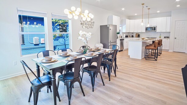 Une cuisine moderne avec des meubles blancs, un îlot central et un coin repas avec une table dressée pour six personnes.