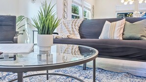 Un salon moderne avec un canapé foncé, une table basse en verre et une plante en pot.