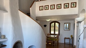 Un vaste espace de vie doté d’une cheminée, d’une table à manger avec des chaises, d’un escalier et offrant une vue sur l’extérieur grâce à une fenêtre.
