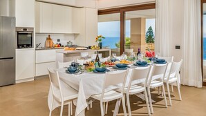 A modern kitchen with white cabinets and a dining area with a table set for six. - Villa Mulberry 10, Emma Villas (Sciacca)