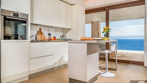 A modern kitchen with a large island, white cabinetry, and a view of the ocean. - Villa Mulberry 10, Emma Villas (Sciacca)