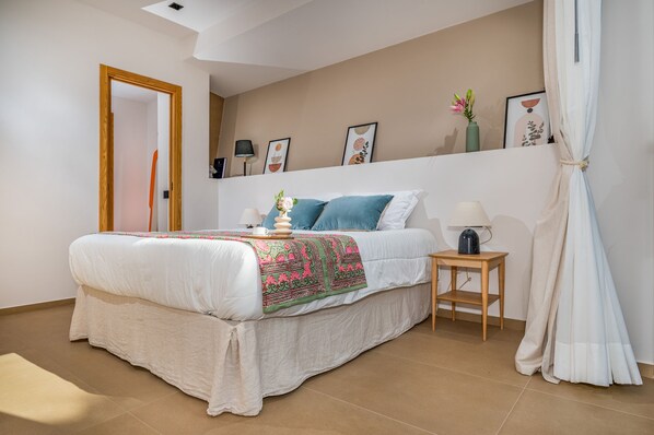 A bedroom with a bed, a bedside table, a lamp, and wall art.