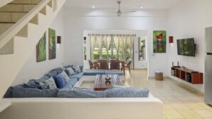 A spacious living room with a large sofa, a dining area, a staircase, and a television.