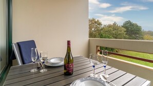 A balcony with a table set for two, a bottle of wine, and a view of a green landscape. - Ferienwohnung in St. Peter-Ording (St. Peter-Ording)