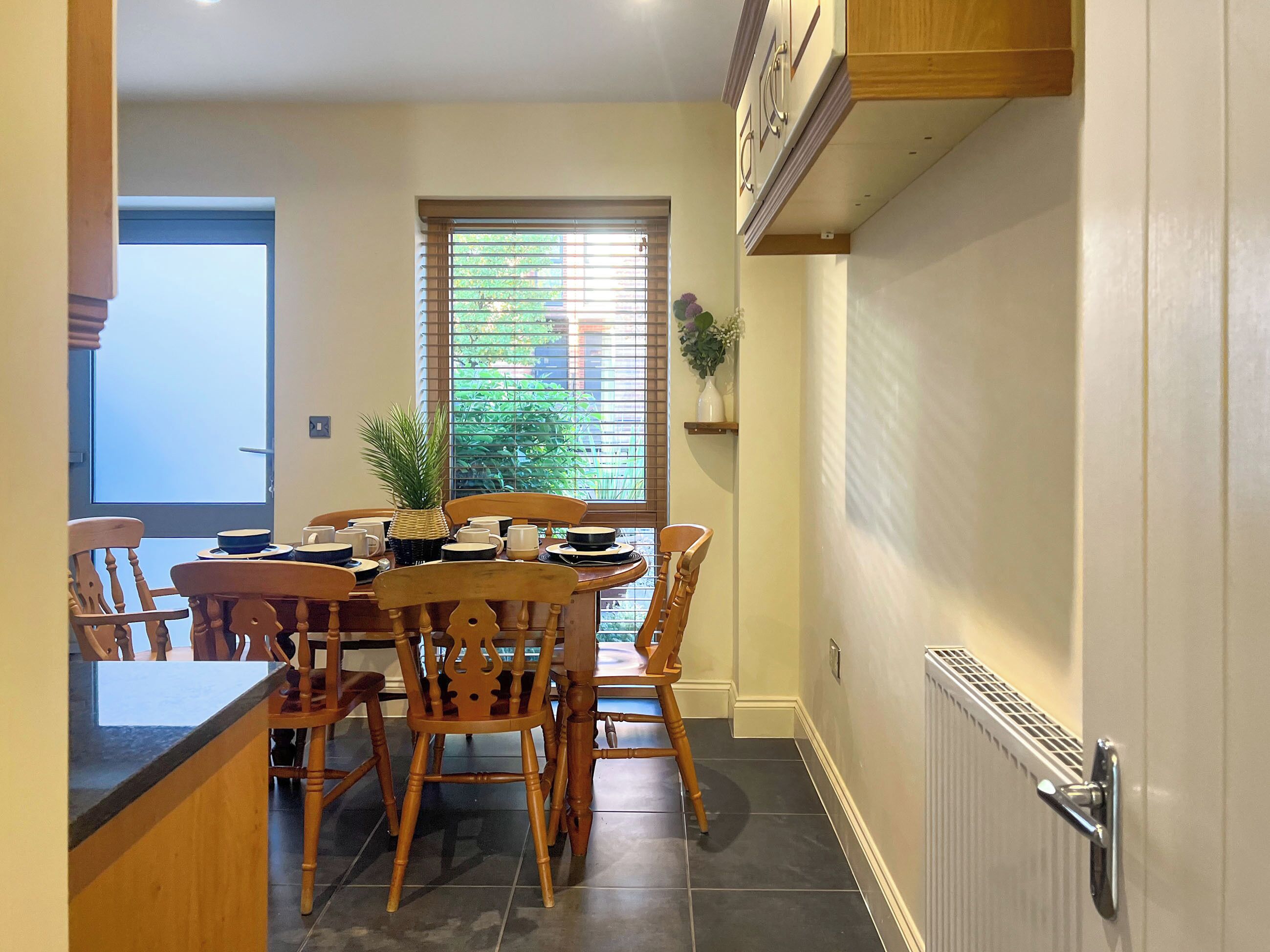 A dining area with a round table, wooden chairs, and a window with blinds.