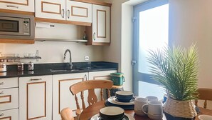 Une cuisine avec des meubles blancs, un four à micro-ondes, un évier et une table à manger avec des chaises. Il y a une fenêtre donnant sur l’extérieur.