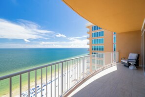 Un balcón con vista a la playa y al océano, una silla y una mesa.