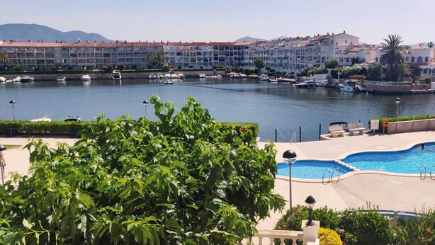 A waterfront hotel with a pool area, boats docked nearby, and a view of the cityscape. - Dream rental, balcony with magnificent pool view (Empuriabrava)