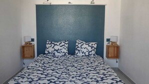 A small, narrow room with a bed centered against a blue wall, flanked by two wooden nightstands with lamps. - Dream rental, balcony with magnificent pool view (Empuriabrava)
