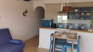 A compact living space with a blue sofa, a small kitchen area with a dining table set, and a decorative wall with circular patterns. - Dream rental, balcony with magnificent pool view (Empuriabrava)