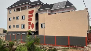 Un edificio de varios pisos con fachada color beige, detalles en rojo y paneles solares en el techo.