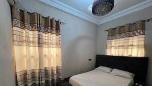 Un dormitorio con cama, cabecera, cortinas y candelabro.