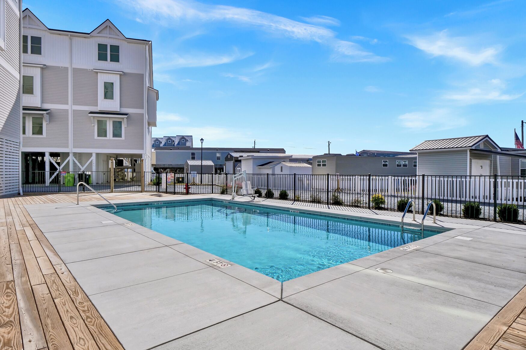 A rectangular swimming pool with a wooden deck surrounding it, set against a backdrop of modern buildings.
