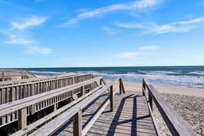 Une promenade en bois menant à une plage, avec des vagues en arrière-plan.