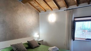 Ein Schlafzimmer mit einer grün gesteppten Bettdecke, zwei Kissen, einem Nachttisch mit Lampe und einem Fenster mit Vorhängen.