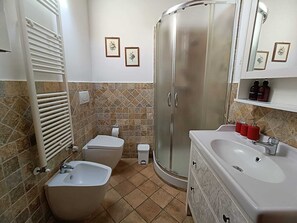 A bathroom with a bidet, toilet, shower, and sink.