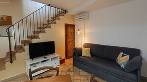 Ein Wohnzimmer mit Treppe, einem Flachbildfernseher, einer Couch und einem Essbereich mit Tisch und Stühlen.