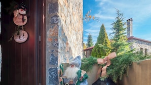 A stone building entrance with a 'WELCOME' mat, a decorative Santa Claus figure, and a rustic lantern.