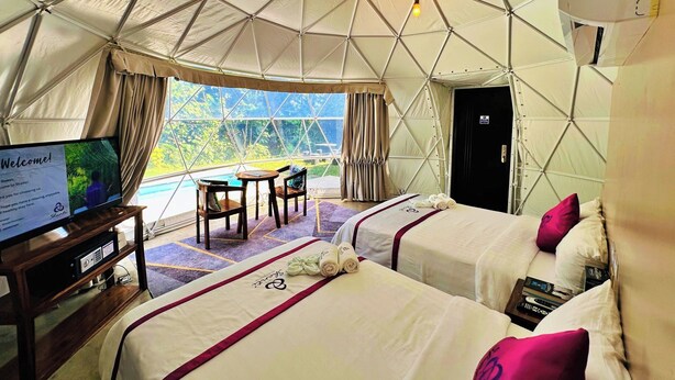 A tent-style accommodation with two beds, a desk, and a TV displaying a welcome message. - Shanti Wellness Sanctuary (Lemery)