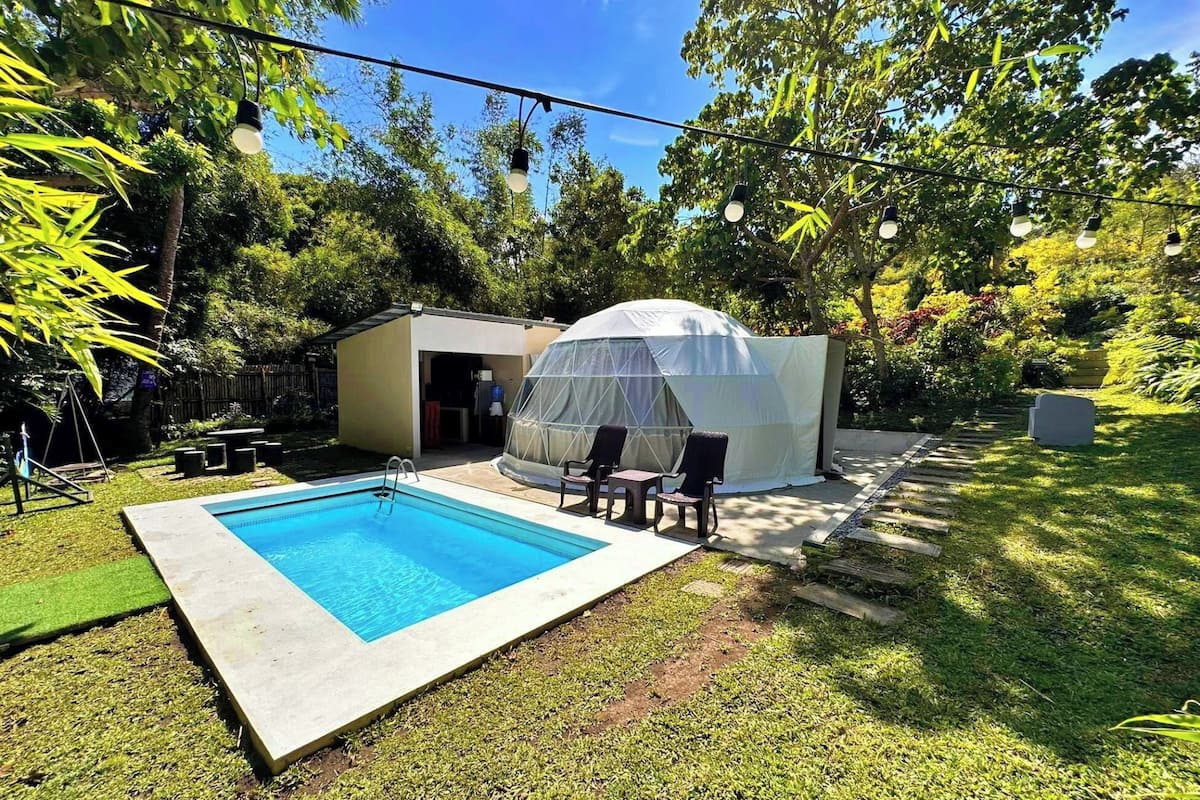 Un jardin avec une piscine, un espace salon couvert et un petit abri de jardin.