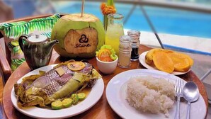 A meal tray with fish, rice, and a drink, set on a table with a view of greenery through a window. - Shanti Wellness Sanctuary (Lemery)