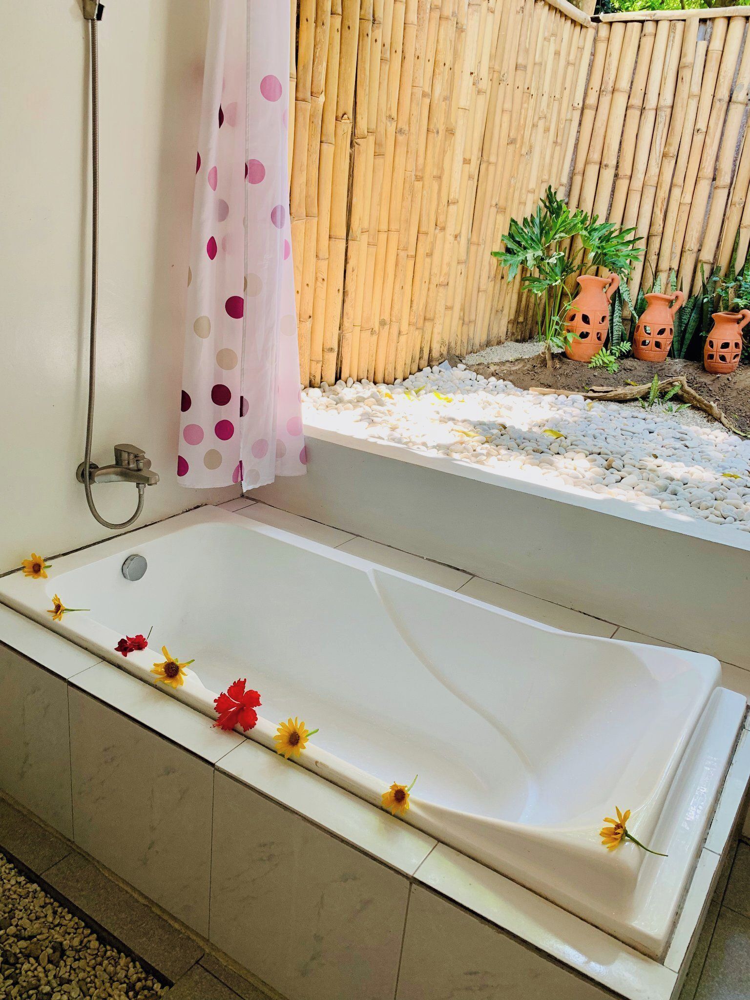 A bathroom with a bathtub, a shower, and a window overlooking a garden with plants and decorative pots.