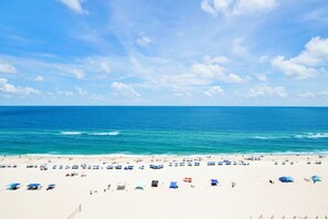A beach with numerous umbrellas and beach chairs, a clear sky, and calm ocean waves. - 🌊White Caps 1502 | Gulf Front | Awesome Amenities🌊 (Orange Beach)