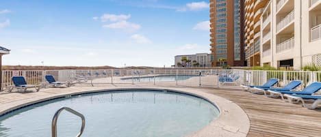 A pool area with lounge chairs and a tall building in the background.