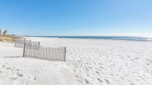 Une plage de sable bordĂ©e dâune clĂŽture en bois, sous un ciel bleu et dĂ©gagĂ©.