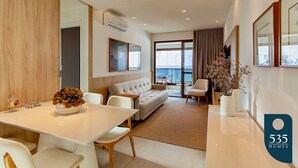 A modern hotel room with a dining area, a sofa, and a view of the sea. - Barra with Sea View - Cozy and Well Decorated (Salvador)