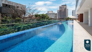 A swimming pool with clear blue water, surrounded by a modern building and a tree. - Barra with Sea View - Cozy and Well Decorated (Salvador)