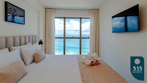 Una habitació d'hotel amb un llit gran, un televisor fixat a la paret i vista al mar per la finestra.