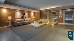 A modern living room with a sofa, coffee table, and chairs, a wooden accent wall, and an elevator. - 2 Bedrooms with Home Office Sea View in Barra (Salvador)