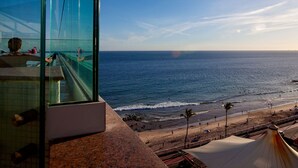 A glass-walled room with a view of the ocean and beach.