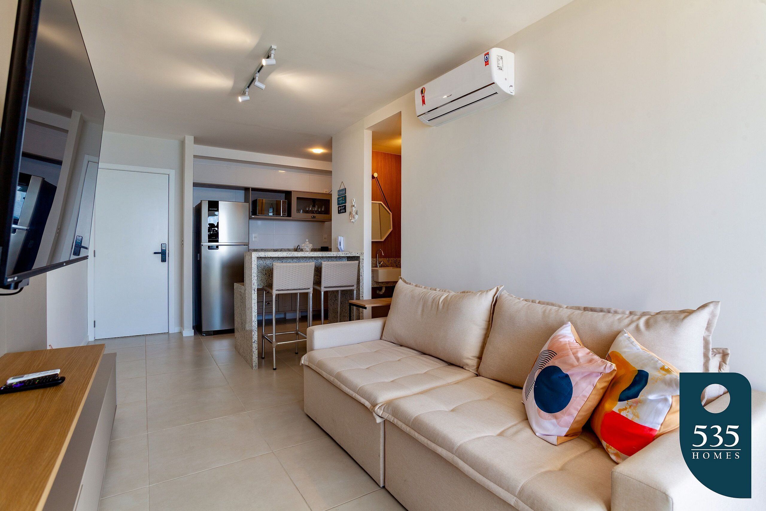 A modern living room with a sofa, a TV, and a kitchen in the background.