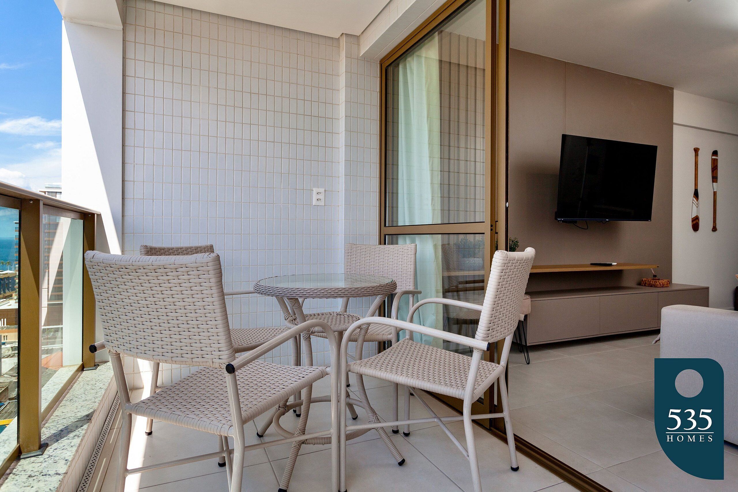 A modern living room with wicker furniture, a flat-screen TV, and a view of the city.