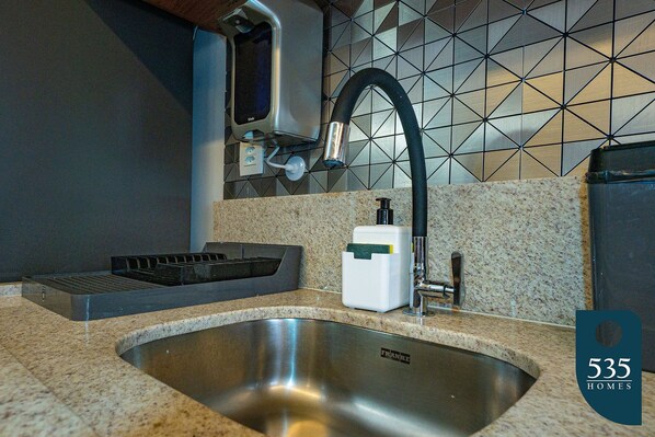 A kitchen with a stainless steel sink, a modern faucet, and a tiled backsplash.