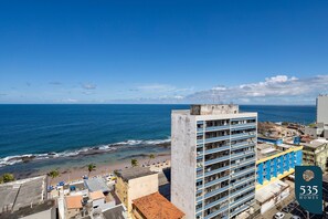 A coastal cityscape with a view of the ocean, featuring a prominent building with multiple balconies and a beach area with umbrellas. - Experience the Charm of Barra Near the Lighthouse (Salvador)