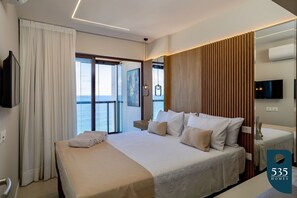 A hotel room with a large bed, a TV, and a view of the sea. - Experience the Charm of Barra Near the Lighthouse (Salvador)