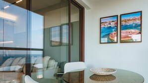 Una habitación moderna con una mesa de vidrio, sillas blancas y vistas al mar a través de amplios ventanales.