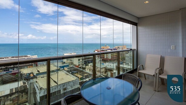 A balcony with a glass railing, a round table, and two chairs.